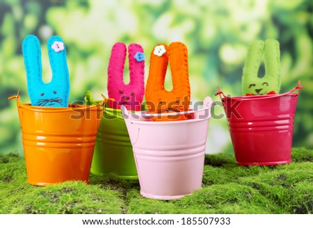 Funny handmade Easter rabbits in pails, on green grass