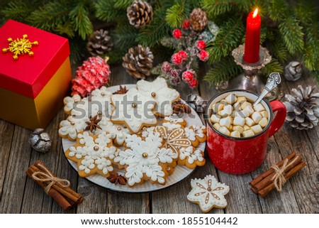Red mug of coffee with marshmallows and gingerbread on a wooden table against a background of fir branches. Christmas still life.