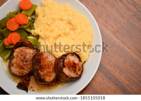 top down closeup of pig medailions with vegetables and polenta with wooden background