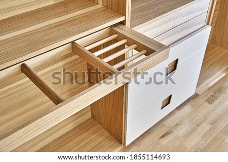 Internal details of the wooden wardrobe with slide out rack for coathangers. Oak veneered plywood cabinets with light gray painted cabinet doors. Detail of modern furniture Royalty-Free Stock Photo #1855114693