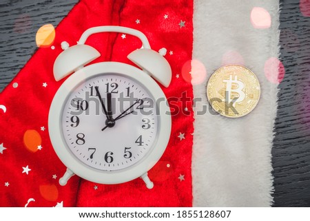 Bitcoin and a white alarm clock lie on Santa's hat, top view. New year's background with bitcoin, cryptocurrency. Problems and growth of the business concept