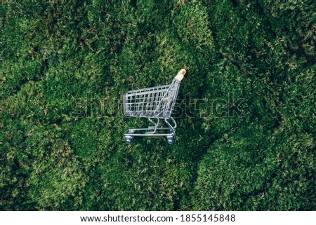 Shopping cart on green grass, moss background. Top view. Minimalism style. Creative design. Shop trolley. Sale, discount, shopaholism, ecology concept. Sustainable lifestyle, conscious consumption. Royalty-Free Stock Photo #1855145848