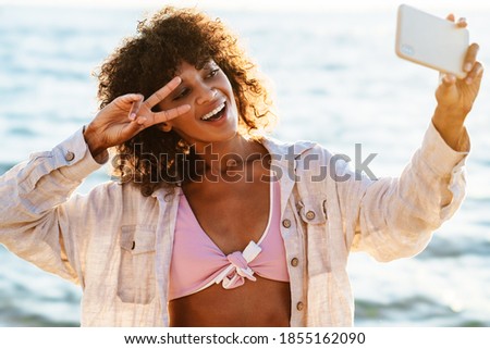 Close up of cheerful young african girl taking a selfie at the beach