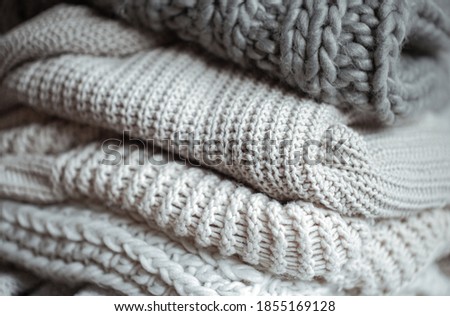 Close up of neatly folded knitted items of pastel color on a light background.