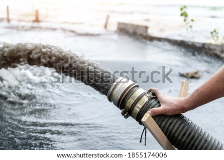 Engeneer hold pipe of power pump machine pouring mud sludge waste water with sand silt on ground. Sand-wash and coast-depeening. Septic sewage maintenance service. Industrial environment pollution Royalty-Free Stock Photo #1855174006