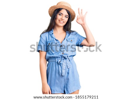 Brunette teenager girl wearing summer hat smiling positive doing ok sign with hand and fingers. successful expression. 