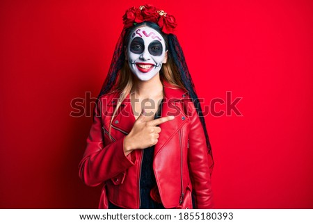 Woman wearing day of the dead costume over red cheerful with a smile of face pointing with hand and finger up to the side with happy and natural expression on face 