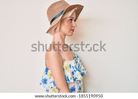 Young blonde woman with tattoo wearing summer hat looking to side, relax profile pose with natural face with confident smile. 