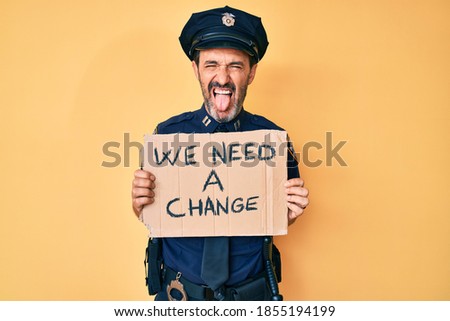 Middle age hispanic man wearing police uniform holding we need a change banner sticking tongue out happy with funny expression. 