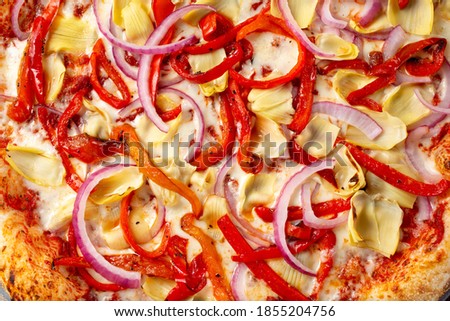 A top down view of a veggie pizza, featuring artichoke, red bell pepper and onion toppings.
