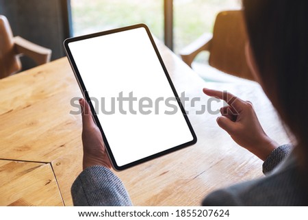Mockup image of a woman holding and pointing finger at digital tablet with blank white desktop screen