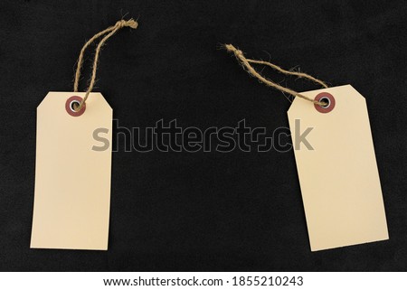 Two blank brown gift tags with a string lying on a black background made of sponge, on the sides.