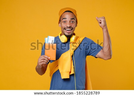 Joyful happy young african american traveler tourist man in basic casual blue t-shirt hat hold passport tickets doing winner gesture isolated on bright yellow colour background, Tattoo translate life