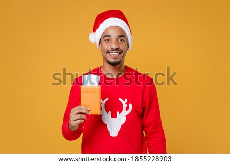 Young fun african traveler tourist Santa man wearing sweater Christmas hat hold passport tickets isolated on yellow background studio. Happy New Year celebration holiday concept Tattoo translate life