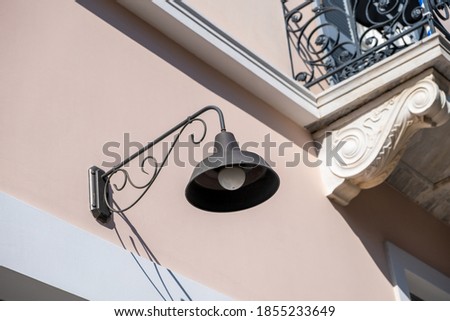 Old fashioned lamp on a neoclassical building facade, Athens Greece. Ornamental retro lantern hanging on wall near balcony over entrance of building on street. 
