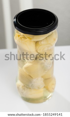 Picture of glass jar with preserved marinated artichokes on table, nobody