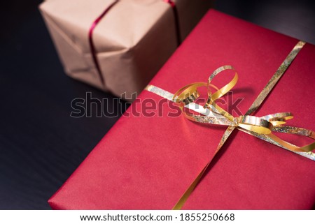Closeup photography of two presents, a red gift with gold ribbon and a kraft present with red ribbon on dark background.