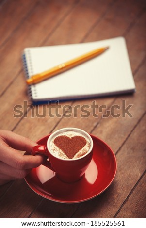 Cup of coffee with shape heart and note with pen on a wooden table.