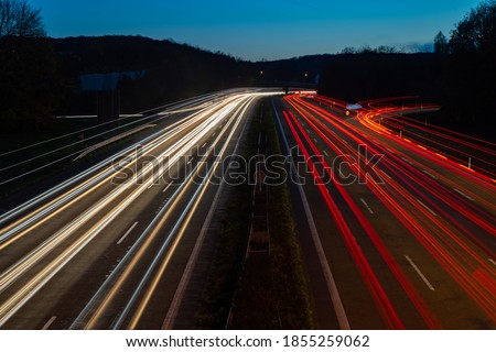 German Autobahn “A1“ in Hagen-West junction at dusk with light traces of passing fast cars and blue evening sky. Long time exposure from a bridge above the six lane highway and white and red lights. Royalty-Free Stock Photo #1855259062