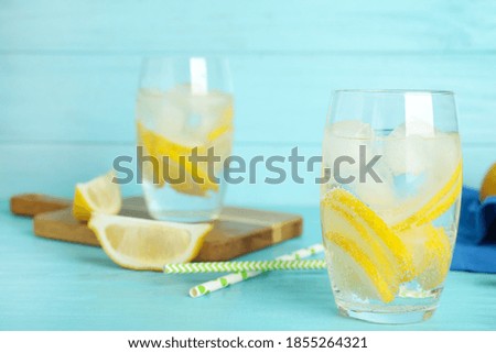 Soda water with lemon slices and ice cubes on light blue wooden table. Space for text