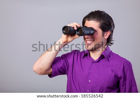 Handsome man with binocular on gray background.
