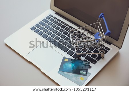 Internet shopping. Modern laptop with small cart and credit cards on light table