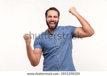 Euphoric thrilled man with beard screaming hurray raising hands up, celebrating his triumph and victory, extremely satisfied with success. Indoor studio shot isolated on white background Royalty-Free Stock Photo #1855298104