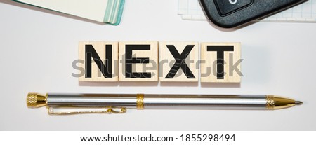 the word next is written on wooden cubes on top of a notebook and on the bottom of a pen. High quality photo