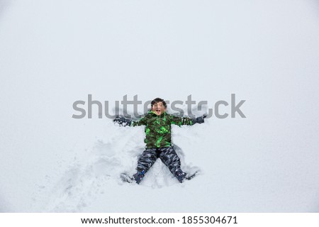 A Happy Asian Boy Making Snow Angel on a White Snow Field.