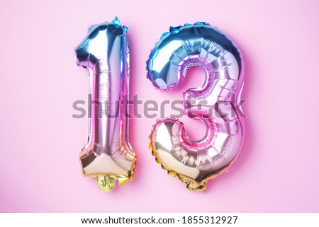 Creative layout. Rainbow foil balloon number, digit thirteen. Birthday greeting card with inscription 13. Anniversary concept. Top view. Stylish colored numeral on pink background. Numerical digit.