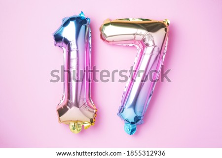 Creative layout. Rainbow foil balloon number, digit seventeen. Birthday greeting card with inscription 17. Anniversary concept. Top view. Stylish colored numeral on pink background. Numerical digit. Royalty-Free Stock Photo #1855312936