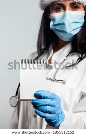 A hospital nurse in a protective mask against COVID-19 SARS-CoV-2 infections holds an empty notebook and a stethoscope