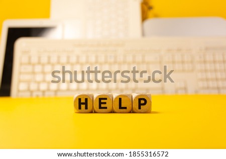 The word help written with dices in front of a yellow background with computers and keyboard
