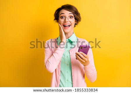 Photo portrait of excited student wearing eyewear keeping smartphone touching cheek amazed isolated on vivid yellow color background