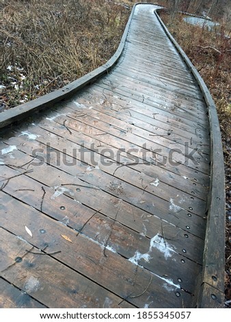 a wooden sidewalk in a wooded park in the fall with a little snow
