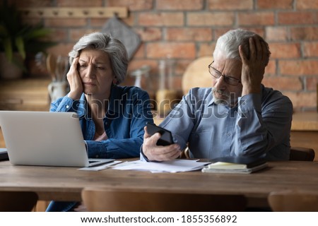 Unhappy mature couple checking financial documents, calculating domestic bills, having problem with money, upset senior man wearing glasses and woman feeling depressed about bankruptcy or debt Royalty-Free Stock Photo #1855356892