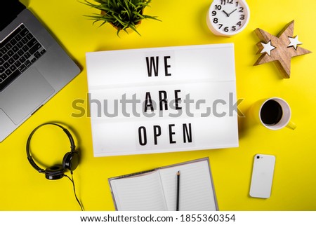 We Are Open text on lightbox on modern yellow office desktop with laptop, smartphone, alarm clock at 10.10 pm, coffee mug, notebook. quarantine opening, isolation end concept
