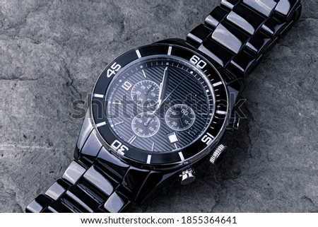 A close up macro shot of a silver metallic watch placed against a grey piece of rock. Soft light, sharp details and a large depth of field.