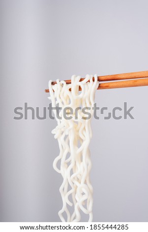 Sideview - eating instant noodle with wooden chopstick over white background.