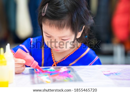 Girl play magic color water drops onto the rainbow cartoon mold. Children do table art. Child hold watercolors. A 3 year old Asian kid wearing a blue shirt.