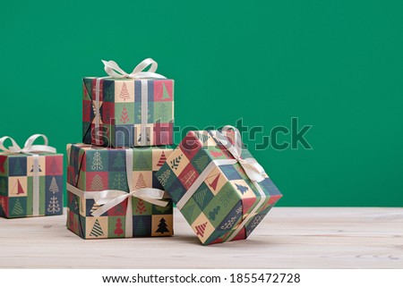Gifts in boxes, wrapped in paper with Christmas and New Year pictures, on a light wooden table, green background.
