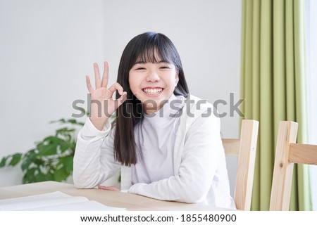 A Japanese junior high school girl smiles in her living room and gives the OK sign