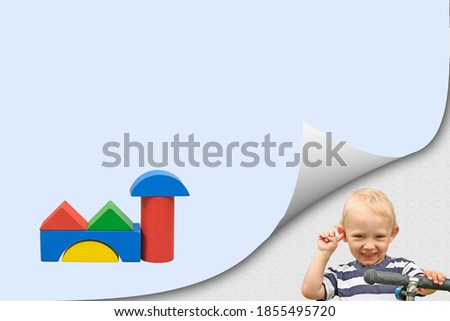 Smiling blond boy in bent corner of the page and colorful building  of wooden cubes on blue blank paper ready for your use.