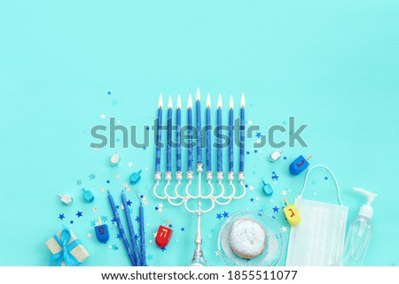 Image of jewish holiday Hanukkah with menorah (traditional Candelabra), donut, wooden dreidel (spinning top). Coronavirus prevention concept, medical mask and and sanitizer gel