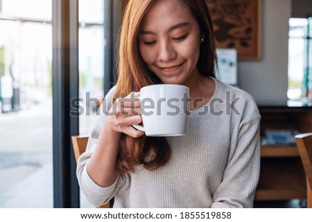 Closeup image of a beautiful young asian woman holding and drinking coffee in cafe