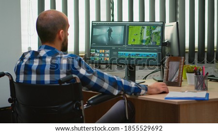 Disabled freelancer videographer editing postproduction a video project creating content sitting in wheelchair in modern company office. Creator blogger working from modern photo studio.