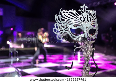 A closeup shot of a mask with a couple dancing in the background