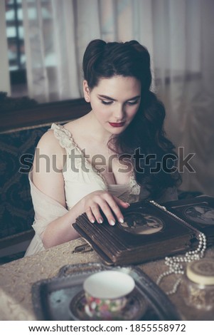 Young woman looks at a photo album. Vintage old style, retro interior.