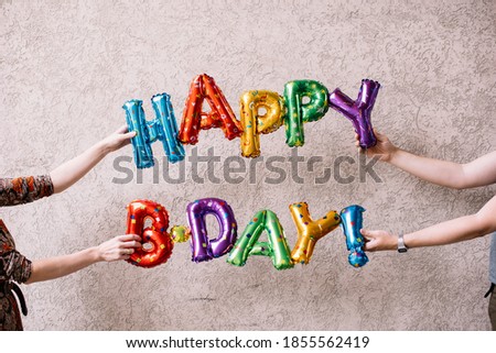 Hands holding inflatable colourful balloons saying "happy birthday" 