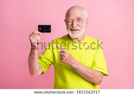 Photo of old cheerful positive smiling man wear lime t-shirt wink eye point finger at credit card isolated on pink color background
